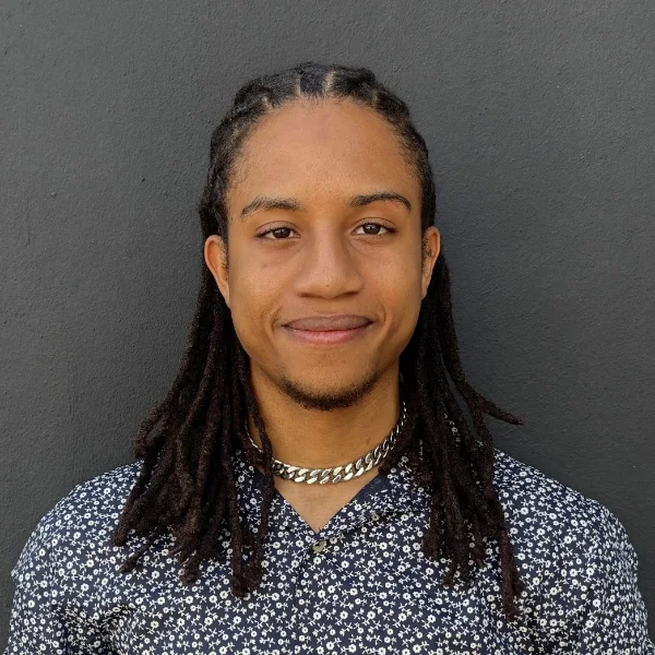 Headshot of Malcolm Daleus, smiling, against a dark grey wall